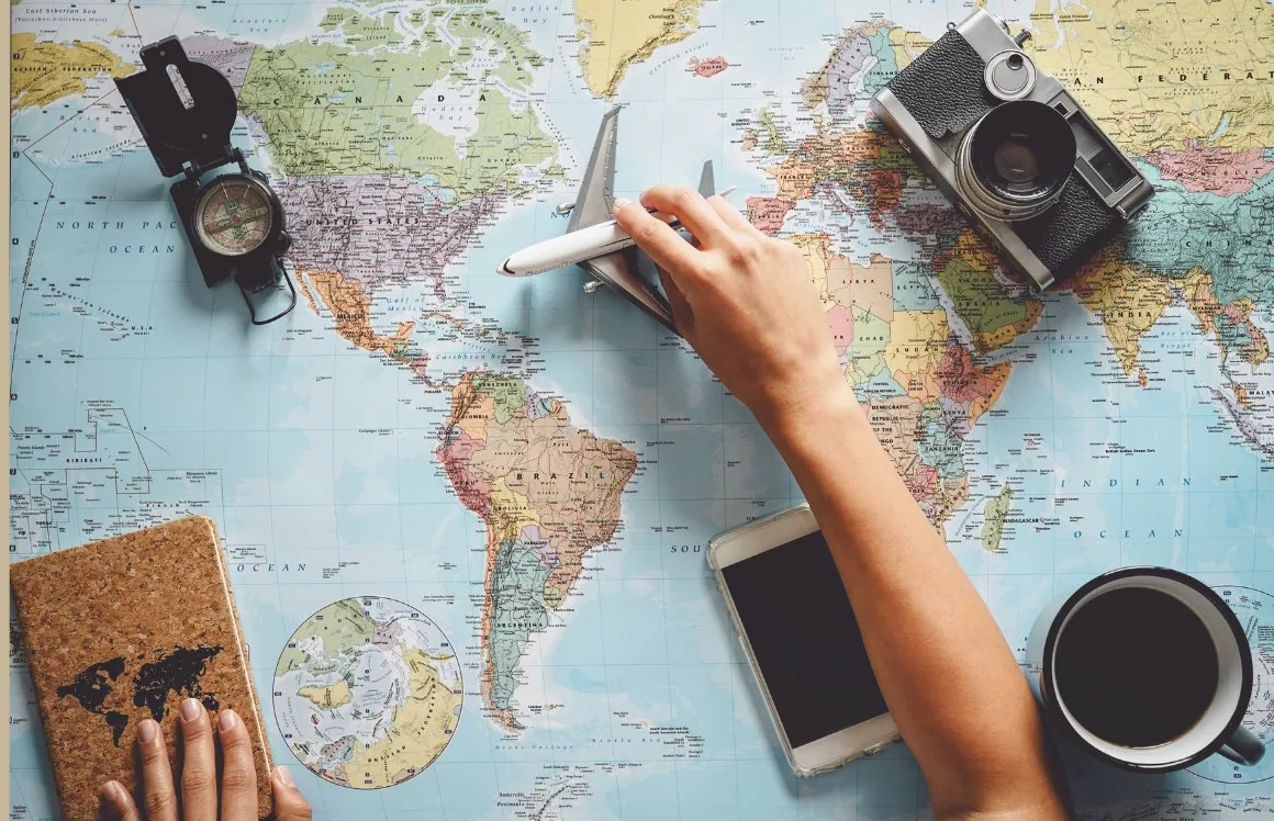 A world map with a model aeroplane, a compass and a camera - planning a travel route